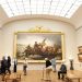 Visitors looking at a large painting in a museum gallery