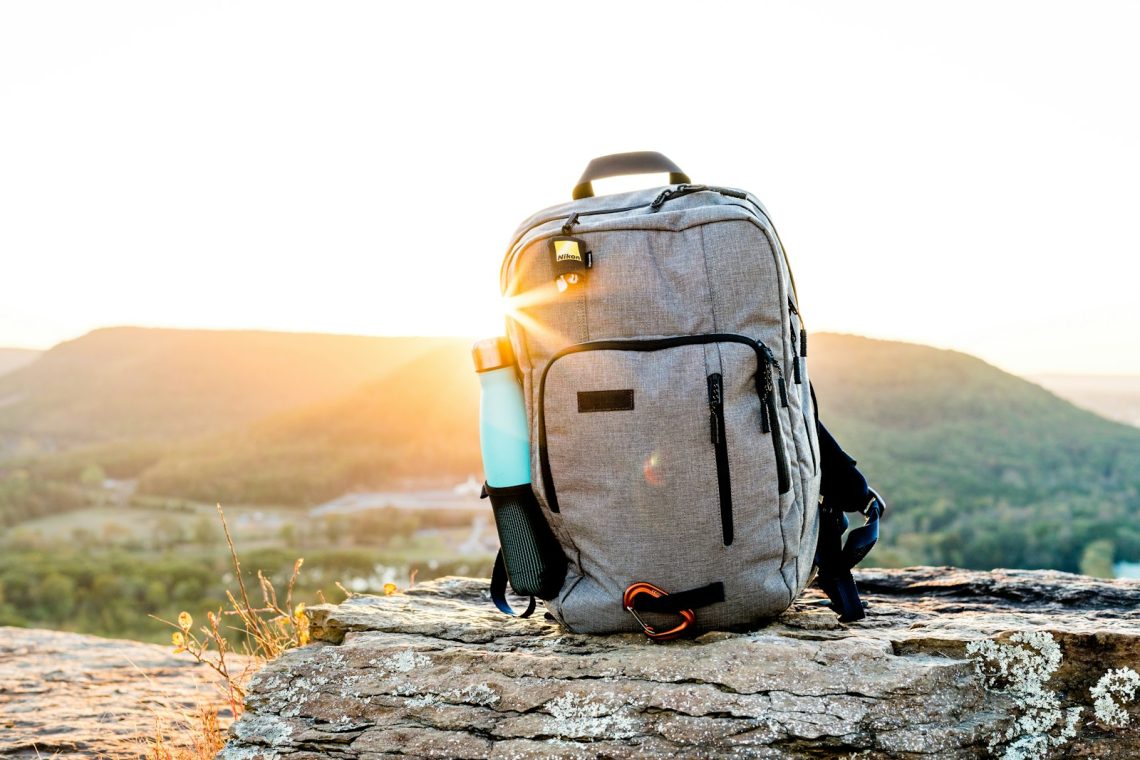 A hiking backpack and water bottle on a rock at sunset