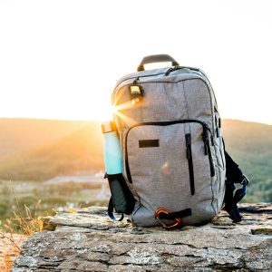 A hiking backpack and water bottle on a rock at sunset