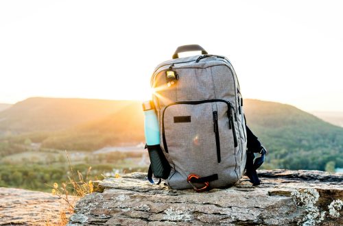 A hiking backpack and water bottle on a rock at sunset