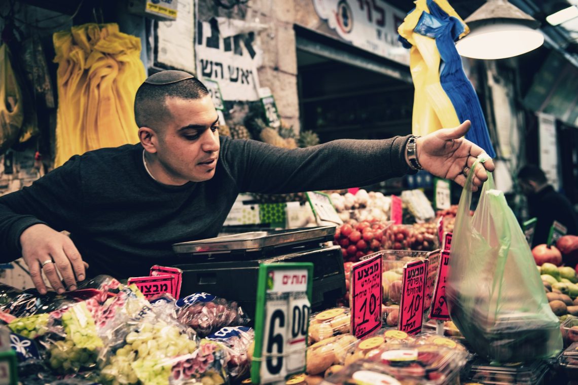 A shopper reaching across a market stall piled with fruit