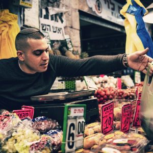 A shopper reaching across a market stall piled with fruit