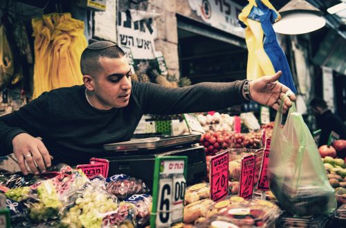 A shopper reaching across a market stall piled with fruit