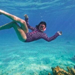 A snorkeler swimming in clear blue water above coral