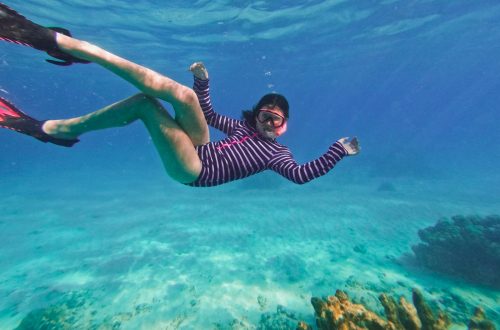 A snorkeler swimming in clear blue water above coral
