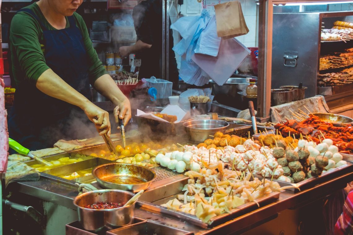 A vendor cooking skewers at a street food stall